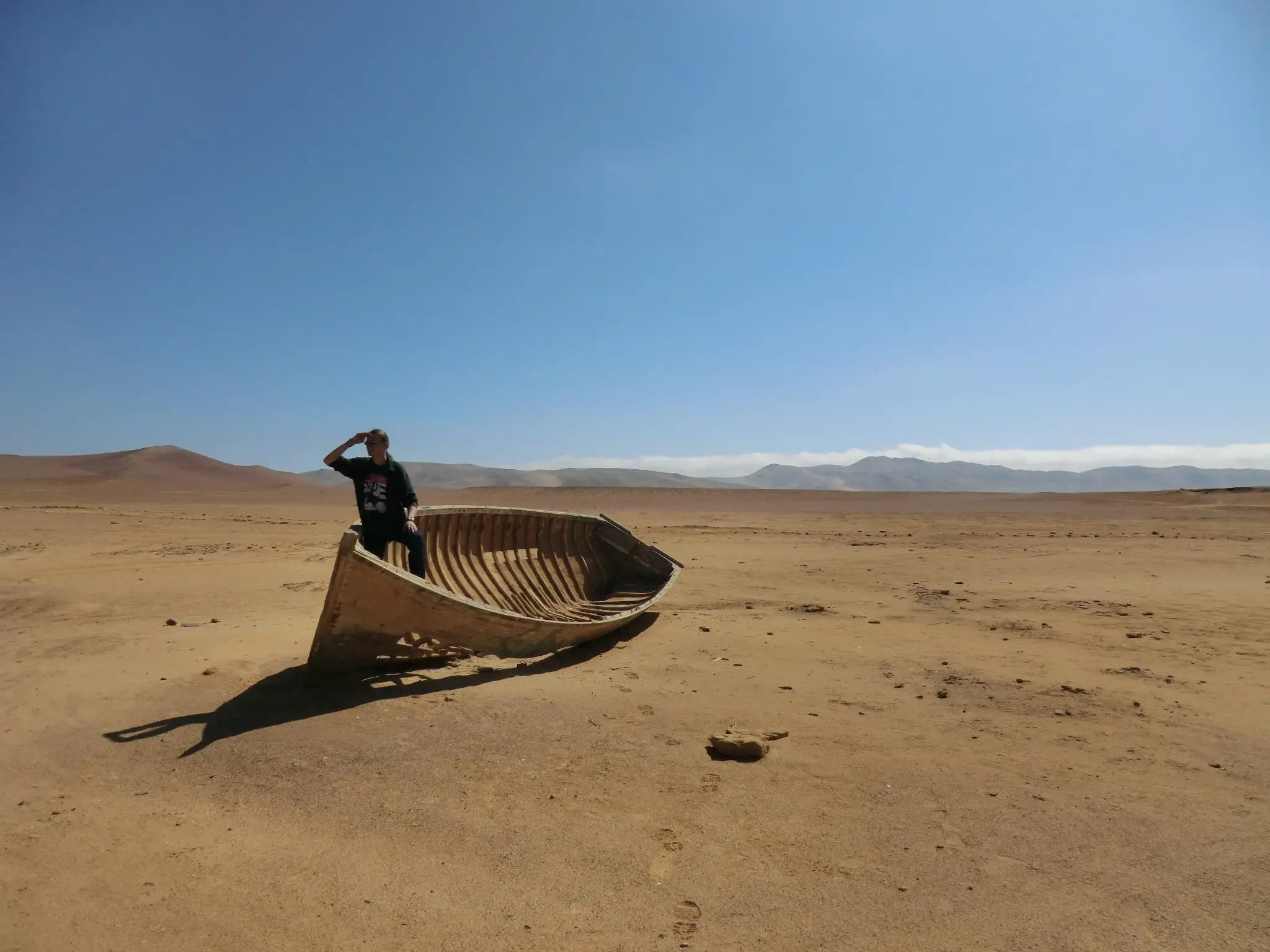 A man standing in a boat in the middle of the desert in Paracas, Peru