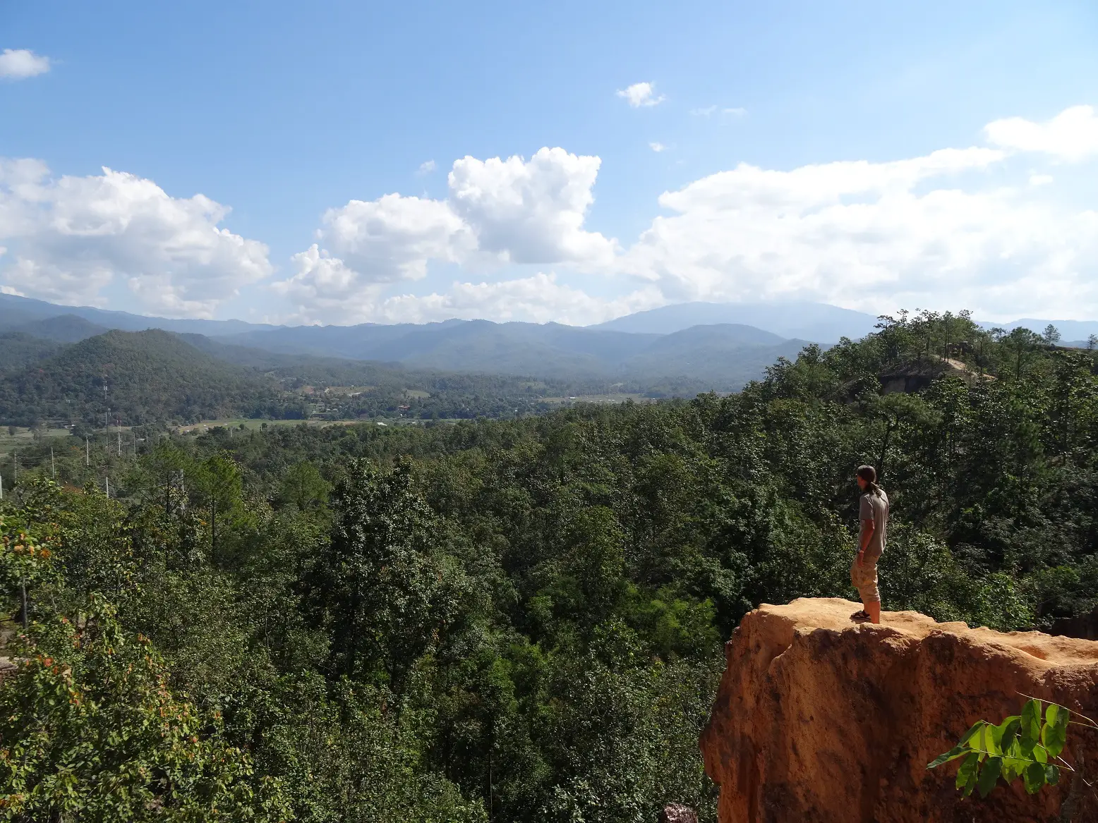 A man standing on a rock outcropping looking into the distance at Pai, Thailand