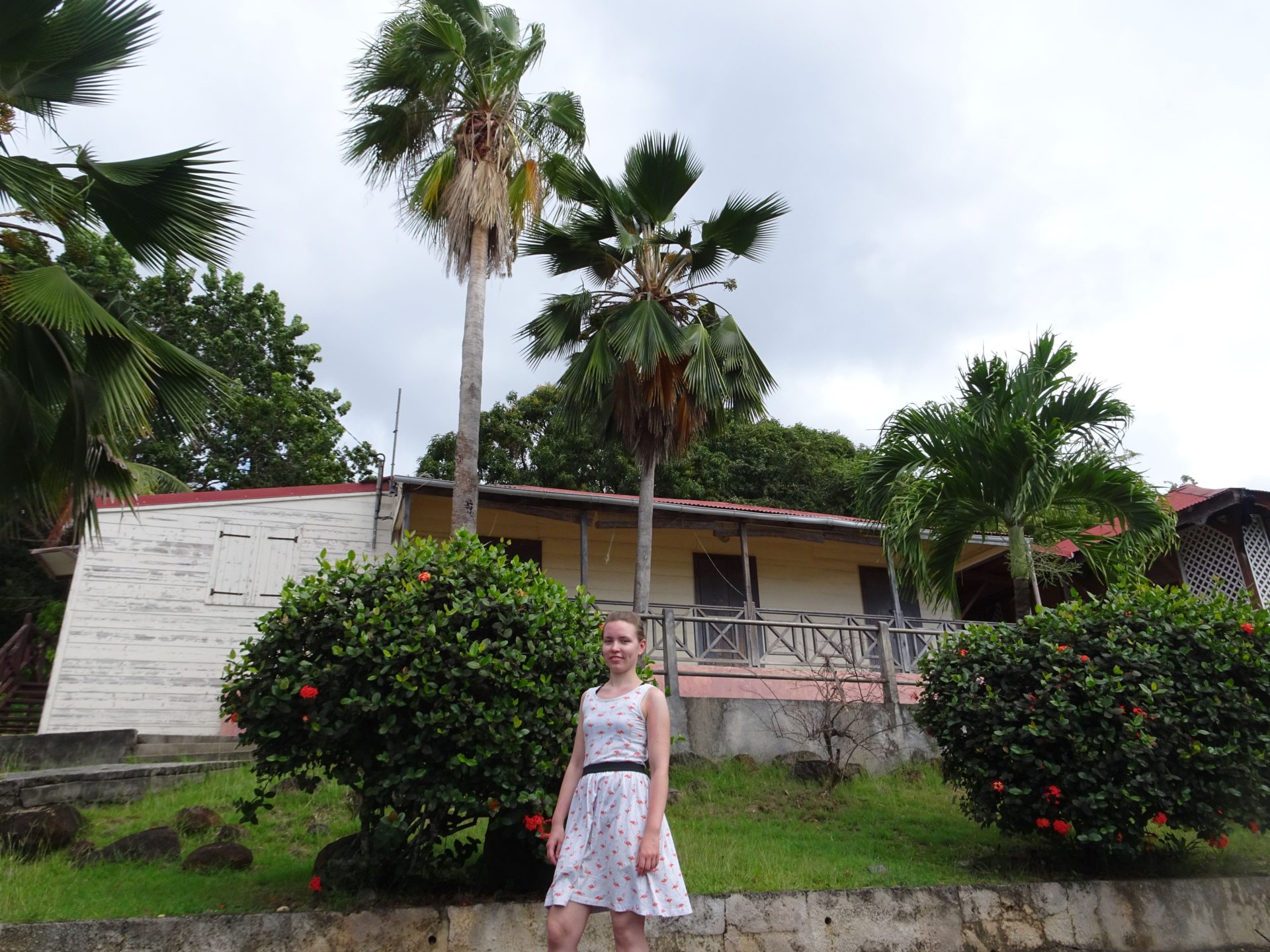 A woman standing in front of a wooden bulding surrounded by palm trees