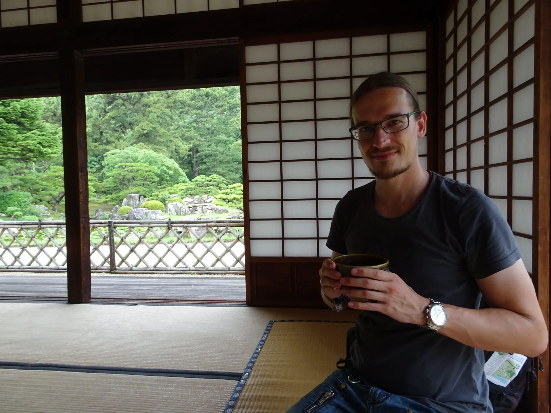 A man holding a cup of tea kneeling on some tatami mats