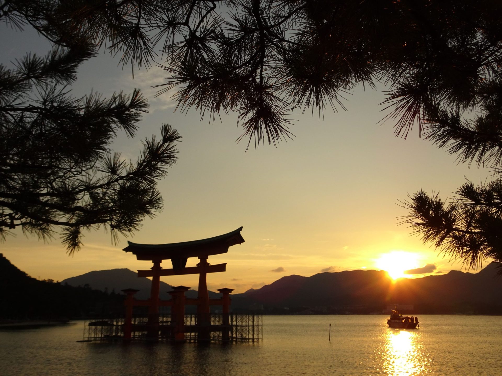 A red wooden gateway in the Ocean with a setting sun in the background and a boat passing
