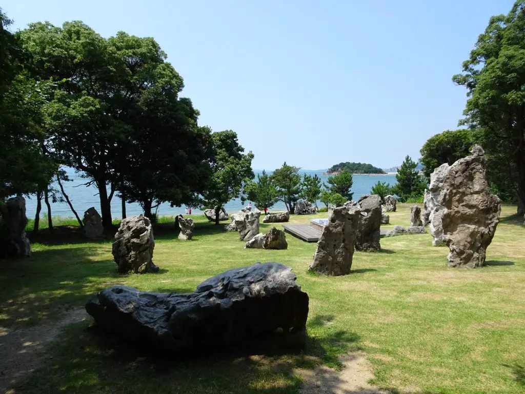 A garden filled with stone sculptures with the ocean in the background
