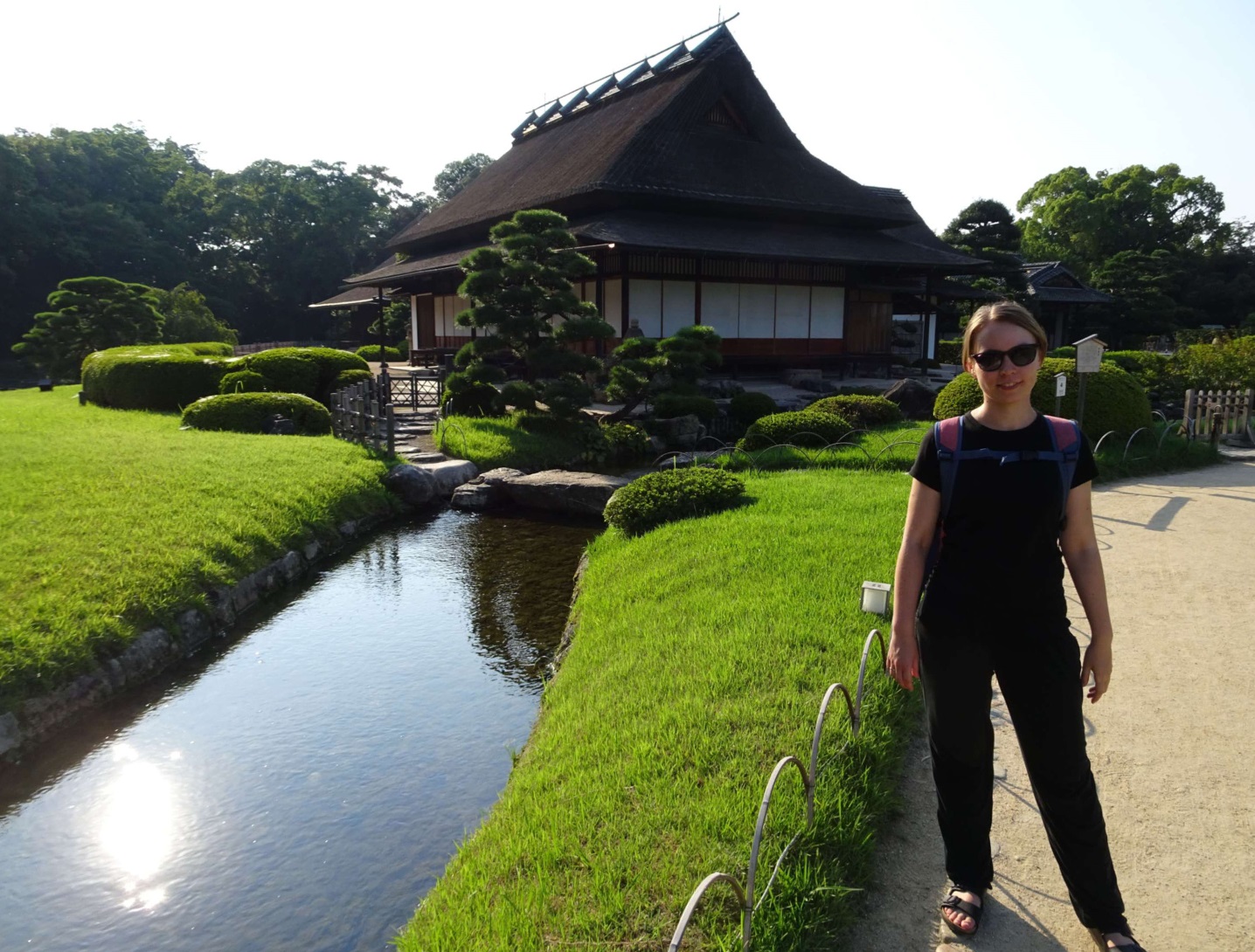 A girl standing near a canal in front of a reet-decked house