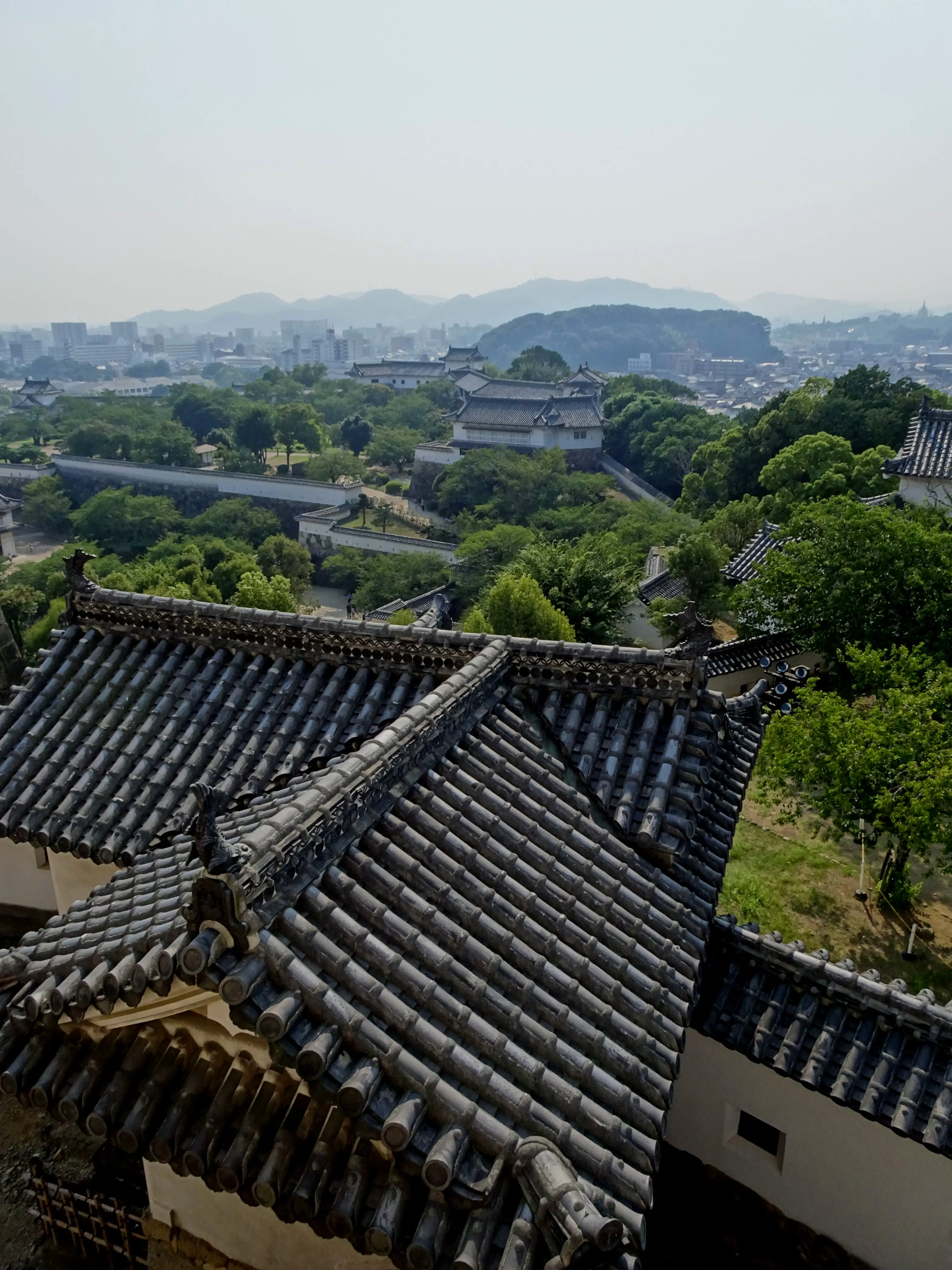 A distant city seen over a garden with glazed roof tiles in the foreground