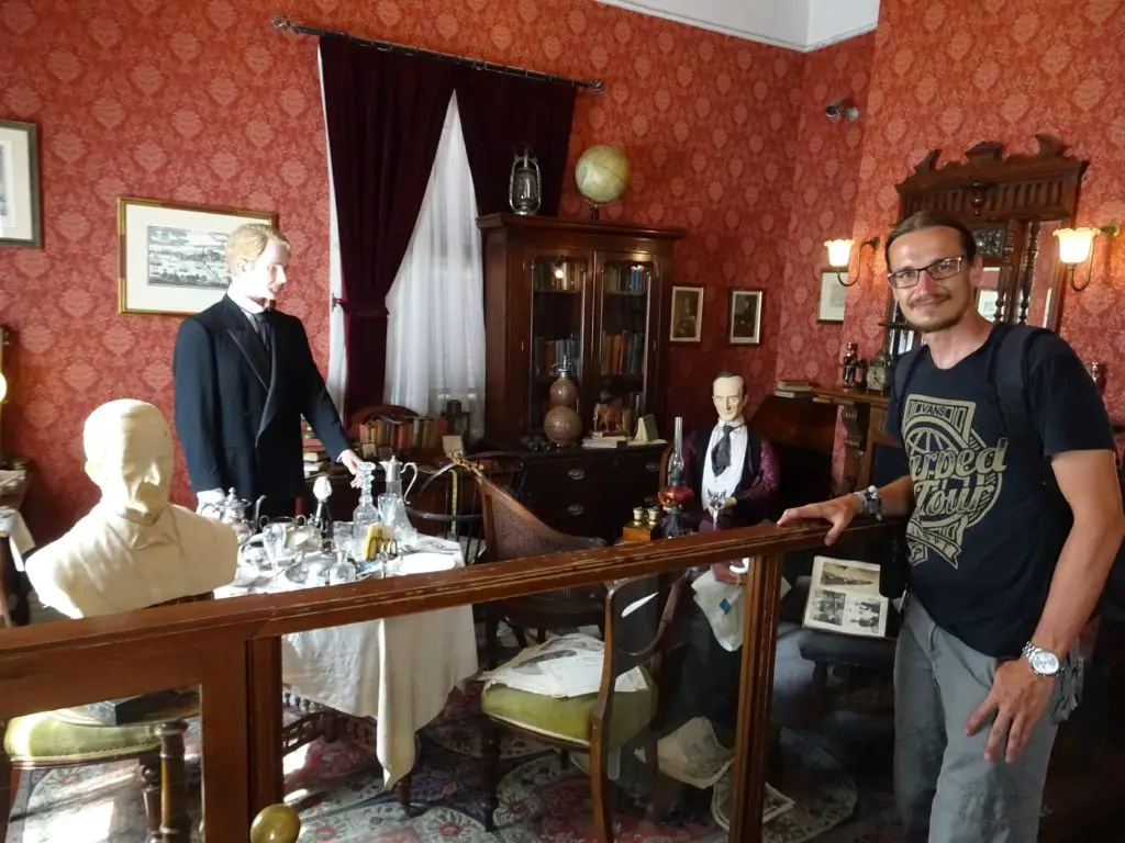 A man standing in a recreation of Sherlock Holmes study with wax figures of Holmes and Watson