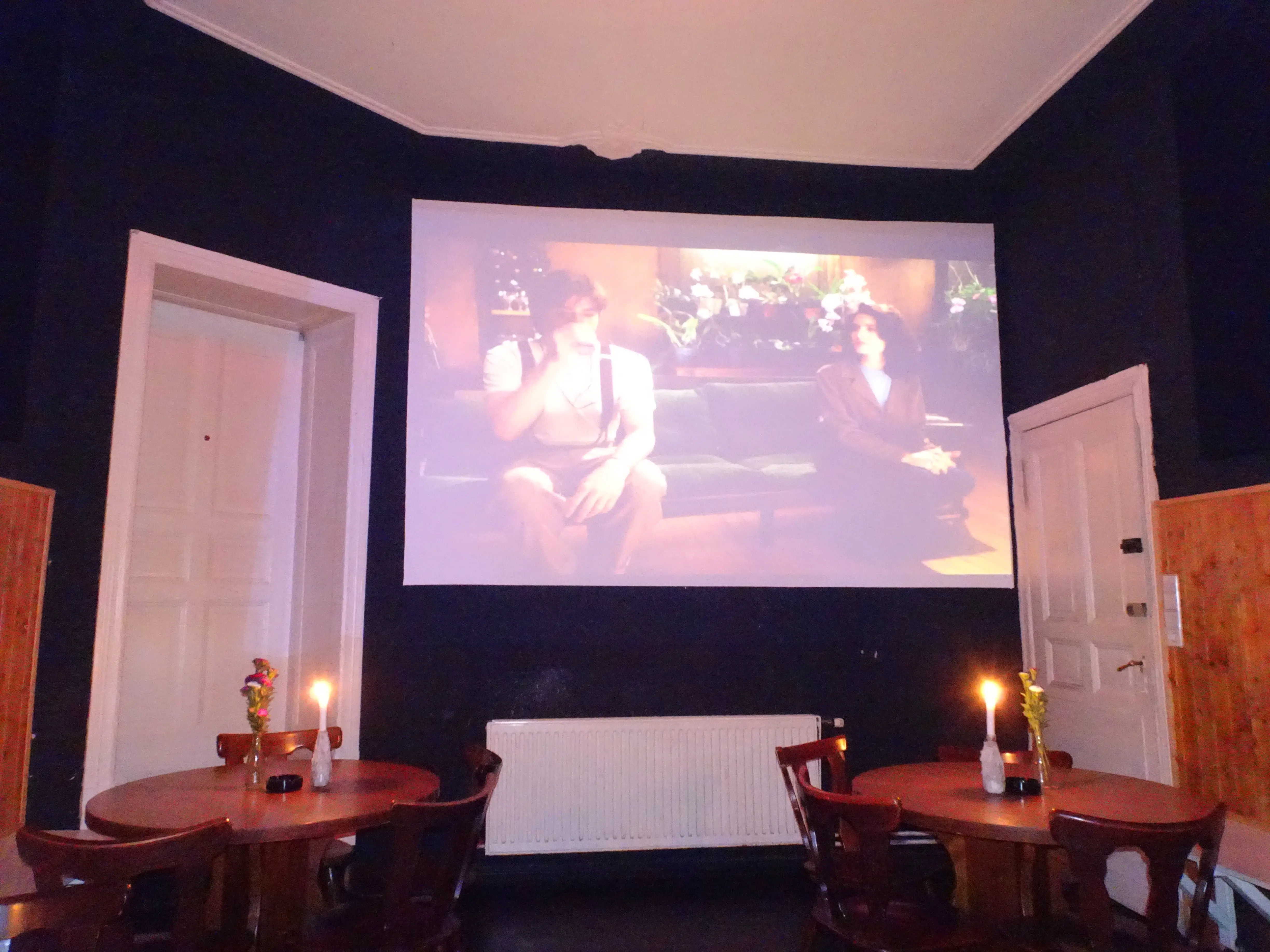 A screen hanging in a restaurant with a movie scene projected on it