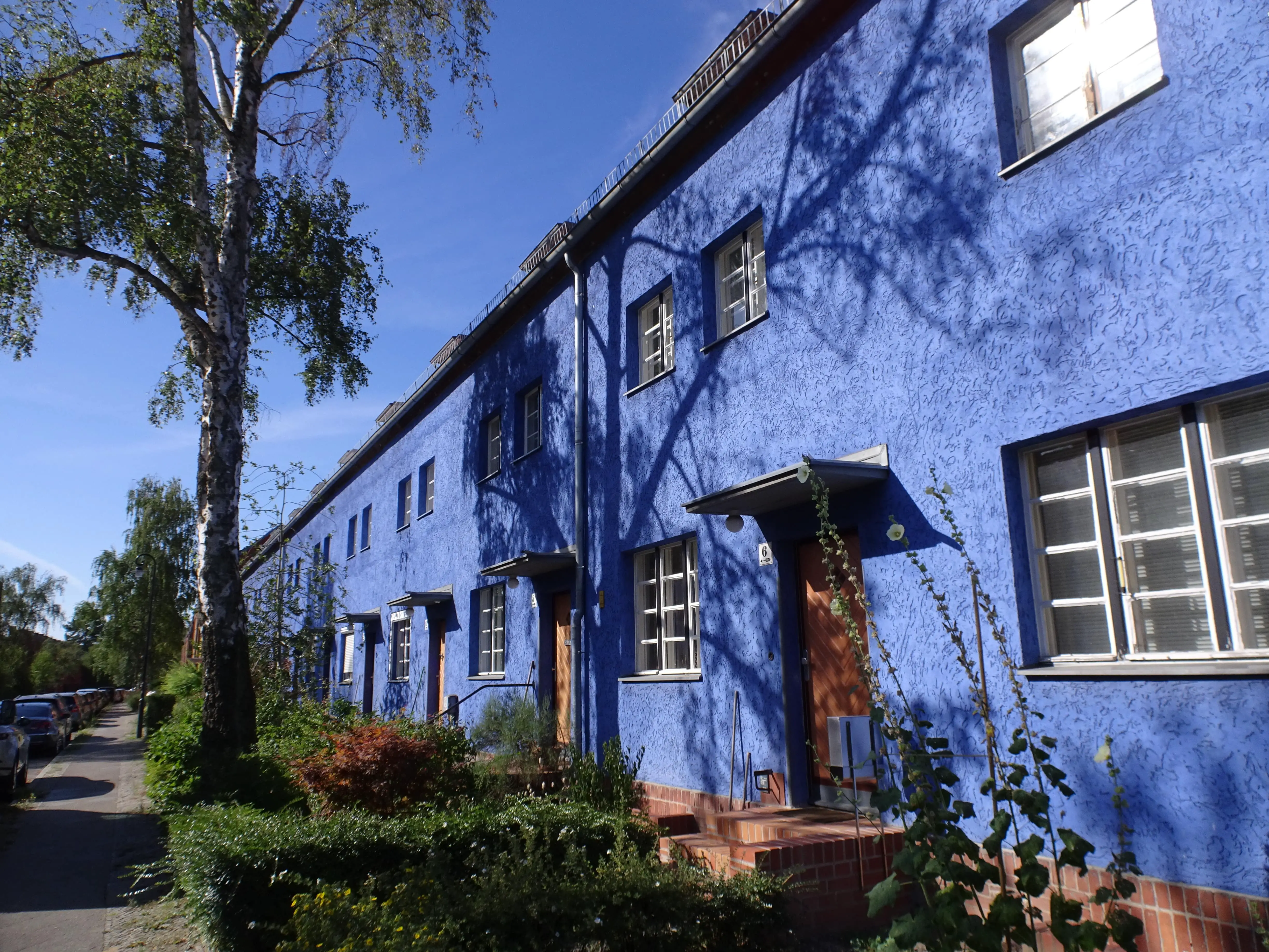 A blue-painted house terrace with small gardens in front