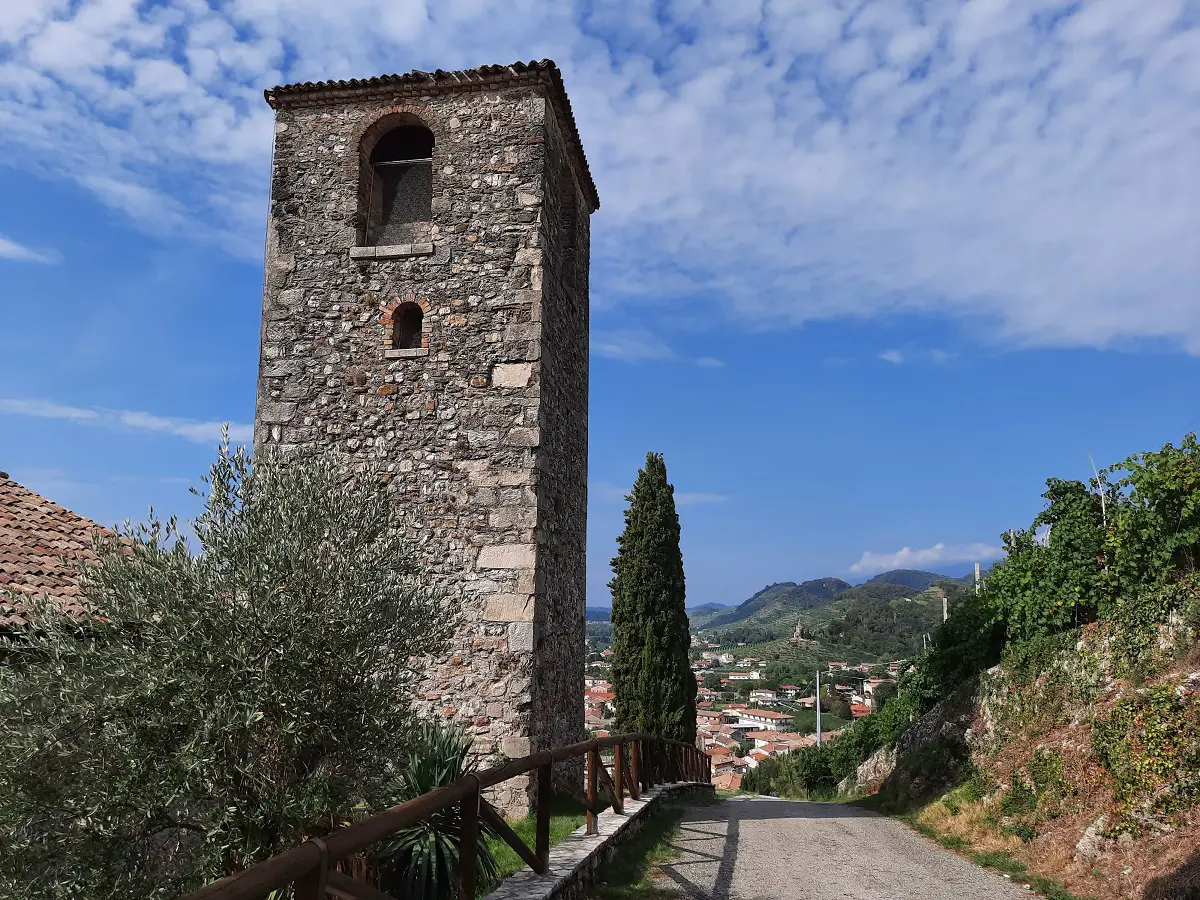 A stone church tower near a cypress tree with a village in the background