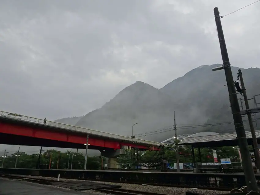 A rural train station backed by mountains shrouded in mist