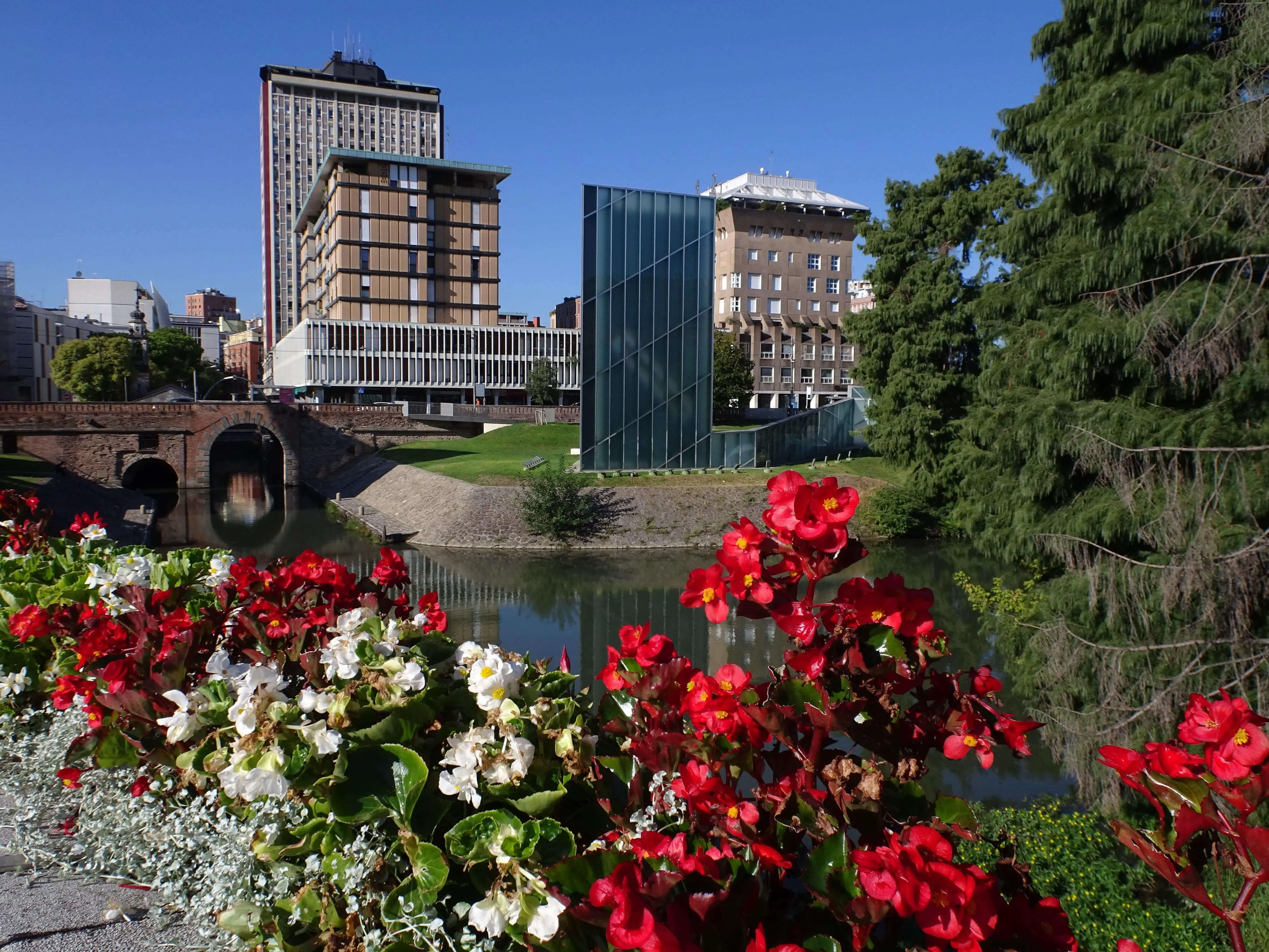 A river surrounded by buildings and seen over a bunch of blooming flowers