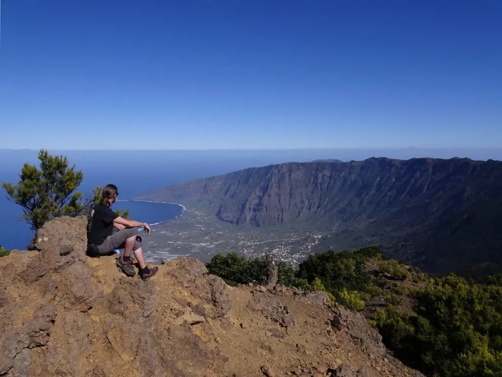 A man sitting on a rock looking out over a valley with the ocean in the background