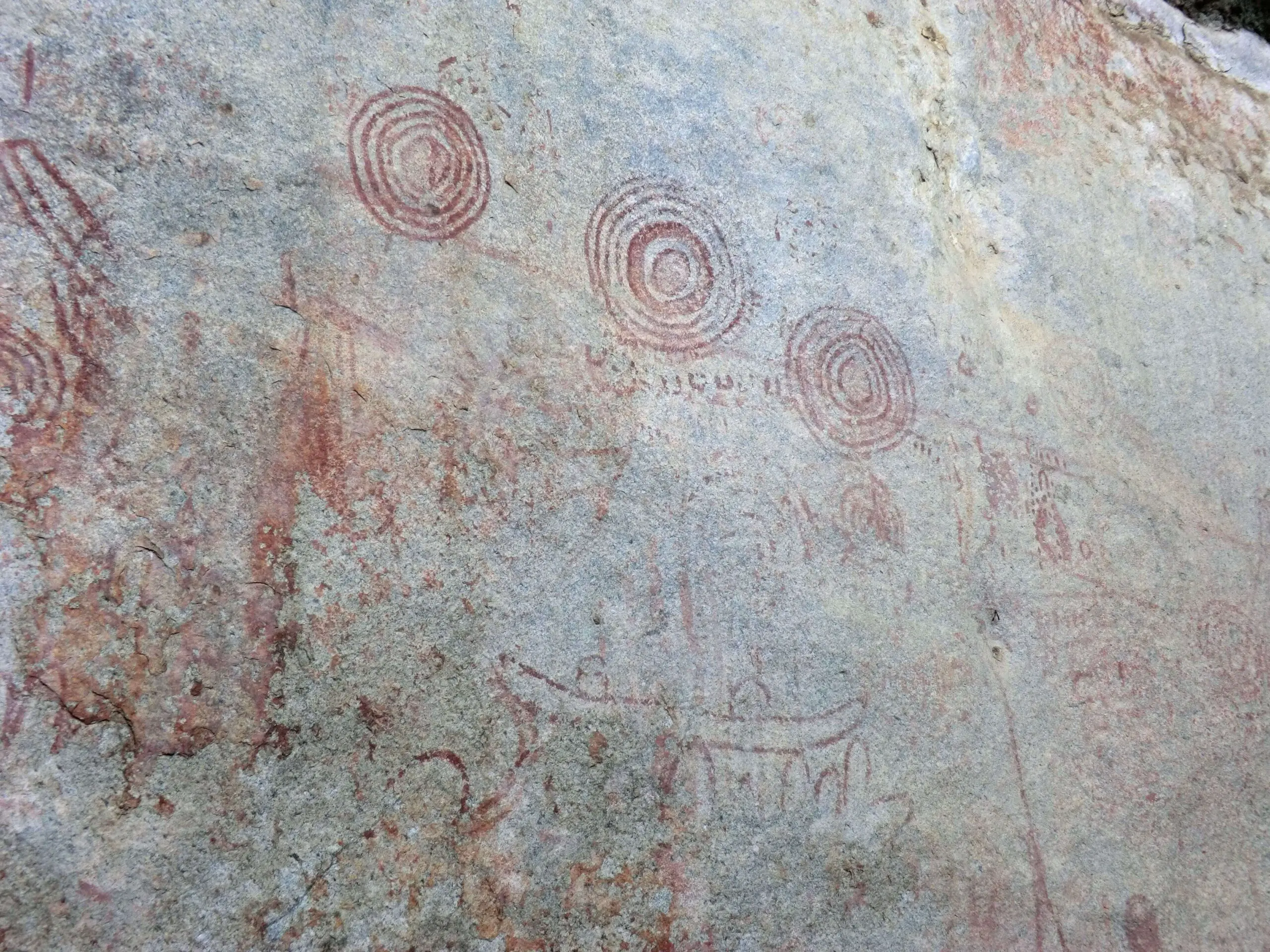 A wall full of red-painted pictographs of figures and concentric circles