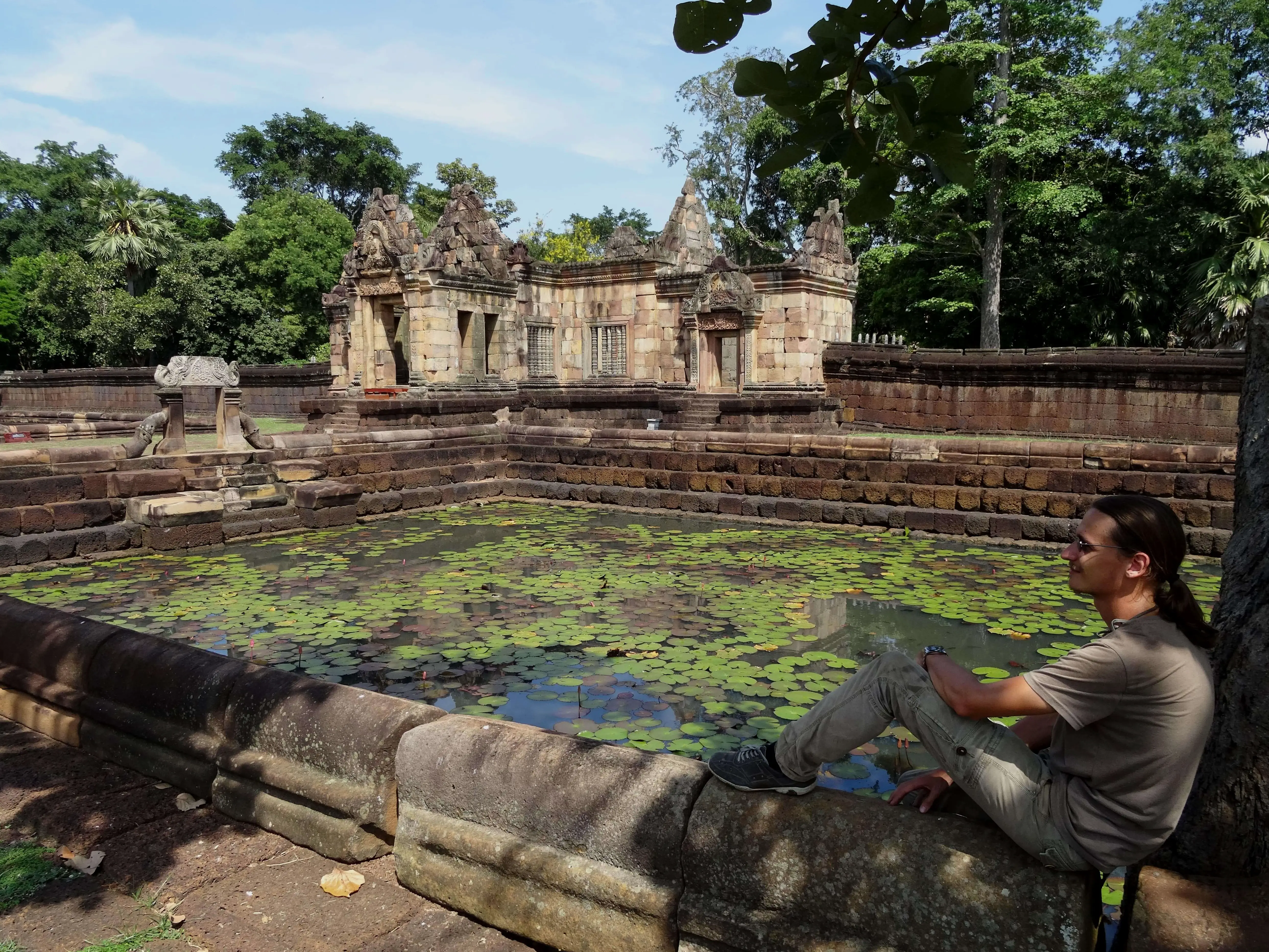 A man sitting next to a pond full of lotus flowers in a ruined temple