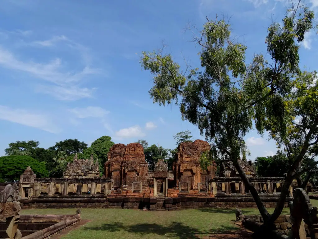 A Khmer temple seen over a green cortyard with a tree in the foreground