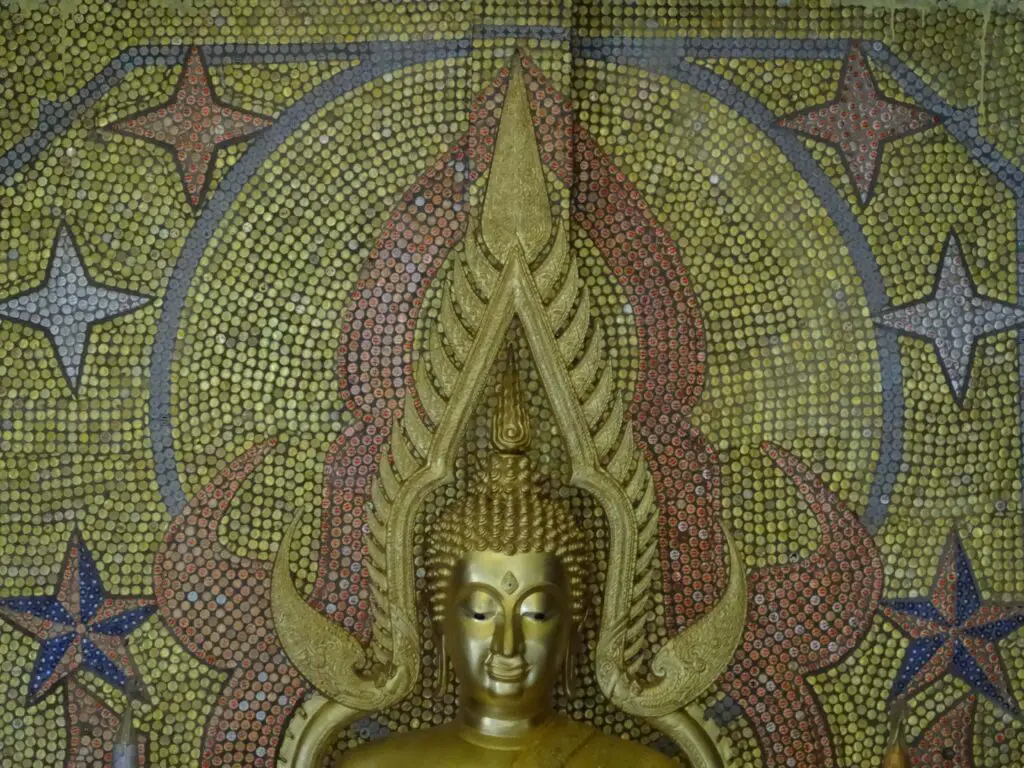 A Buddha Image with a mosaic of bottle caps in the background