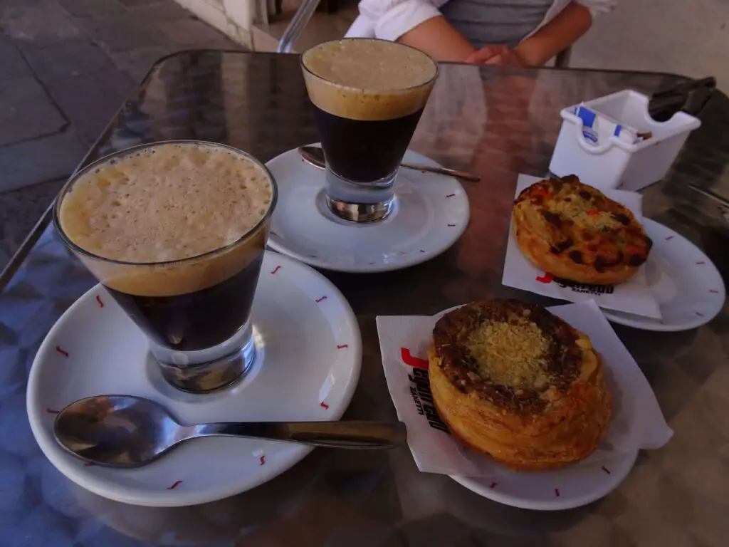 Two coffees and two small pieces of pastry on a table