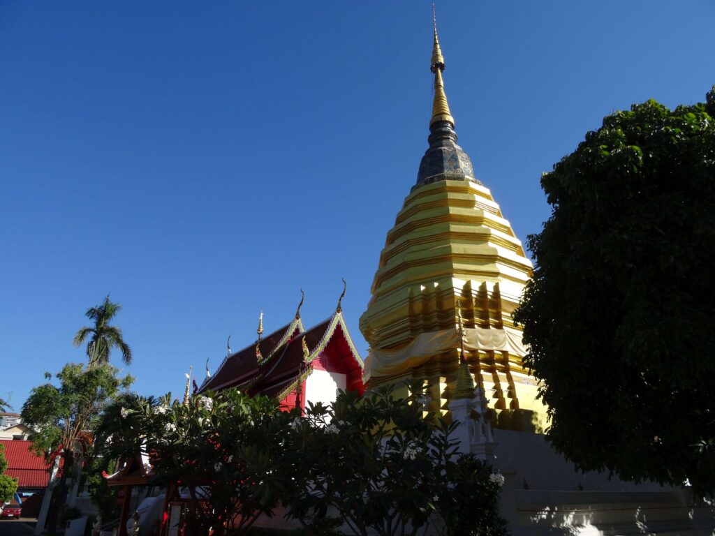 A golden stupa next to a temple building surrounded by trees