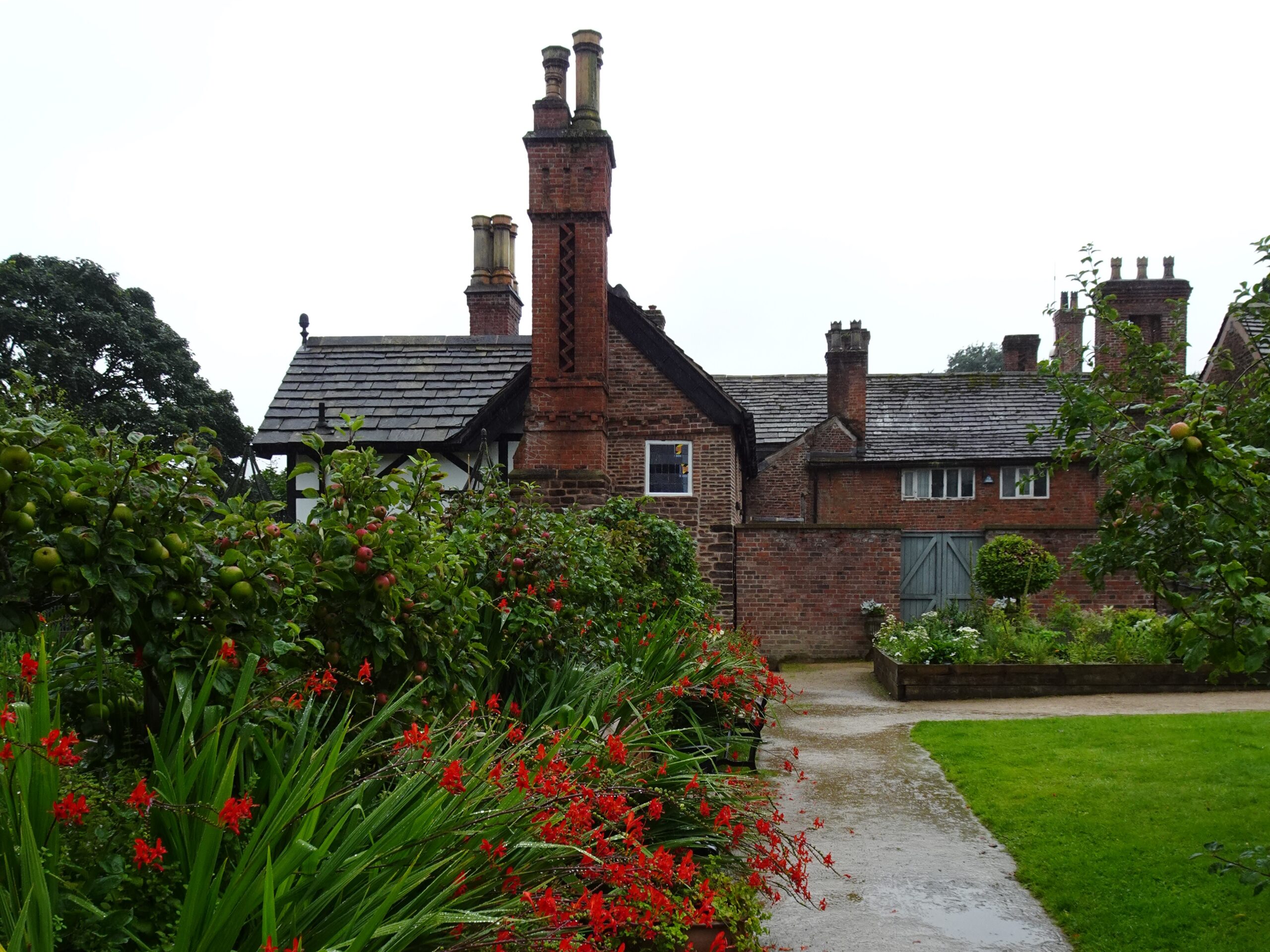 A stately manor with some red-blossomed flowers in the foreground