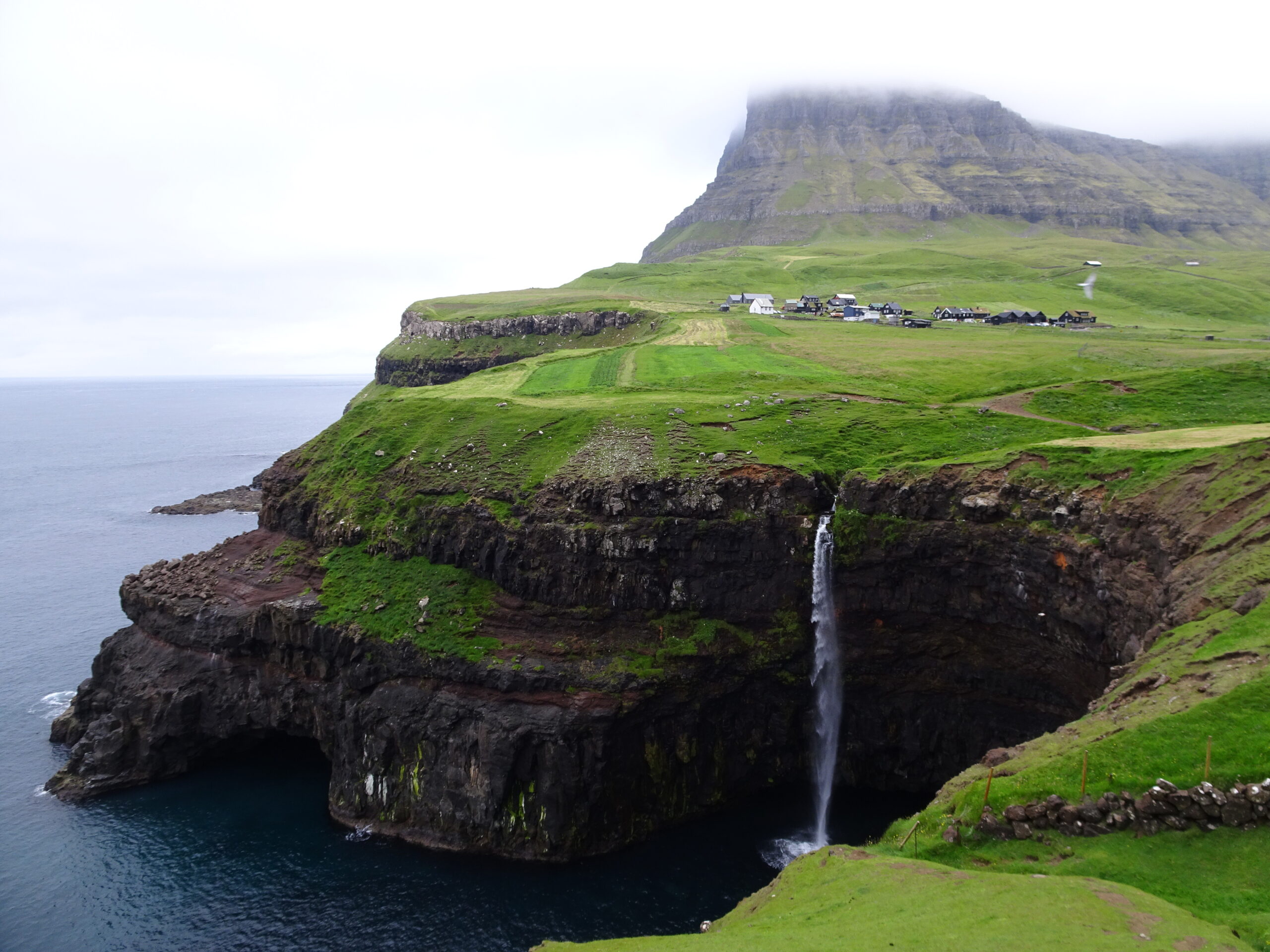 A village by the sea with a waterfall flowing from a tall cliff