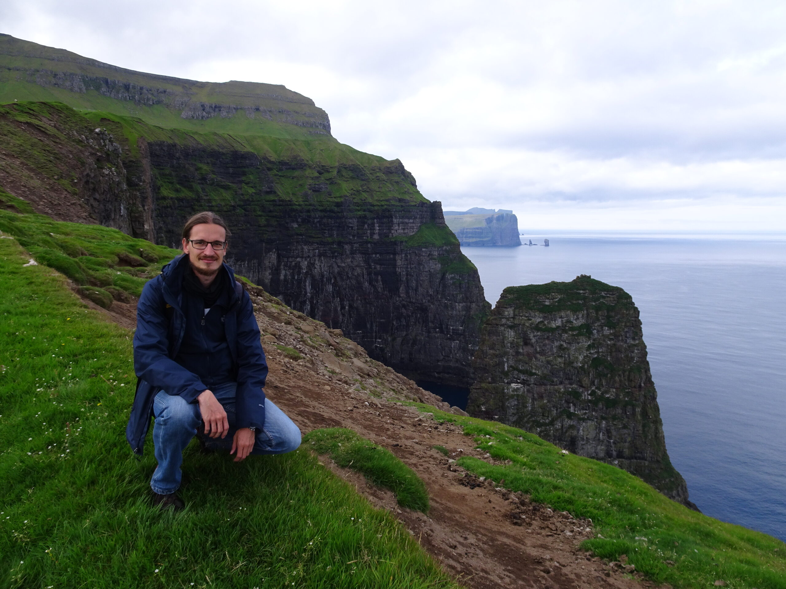 A man crouching on a cliff over the sea