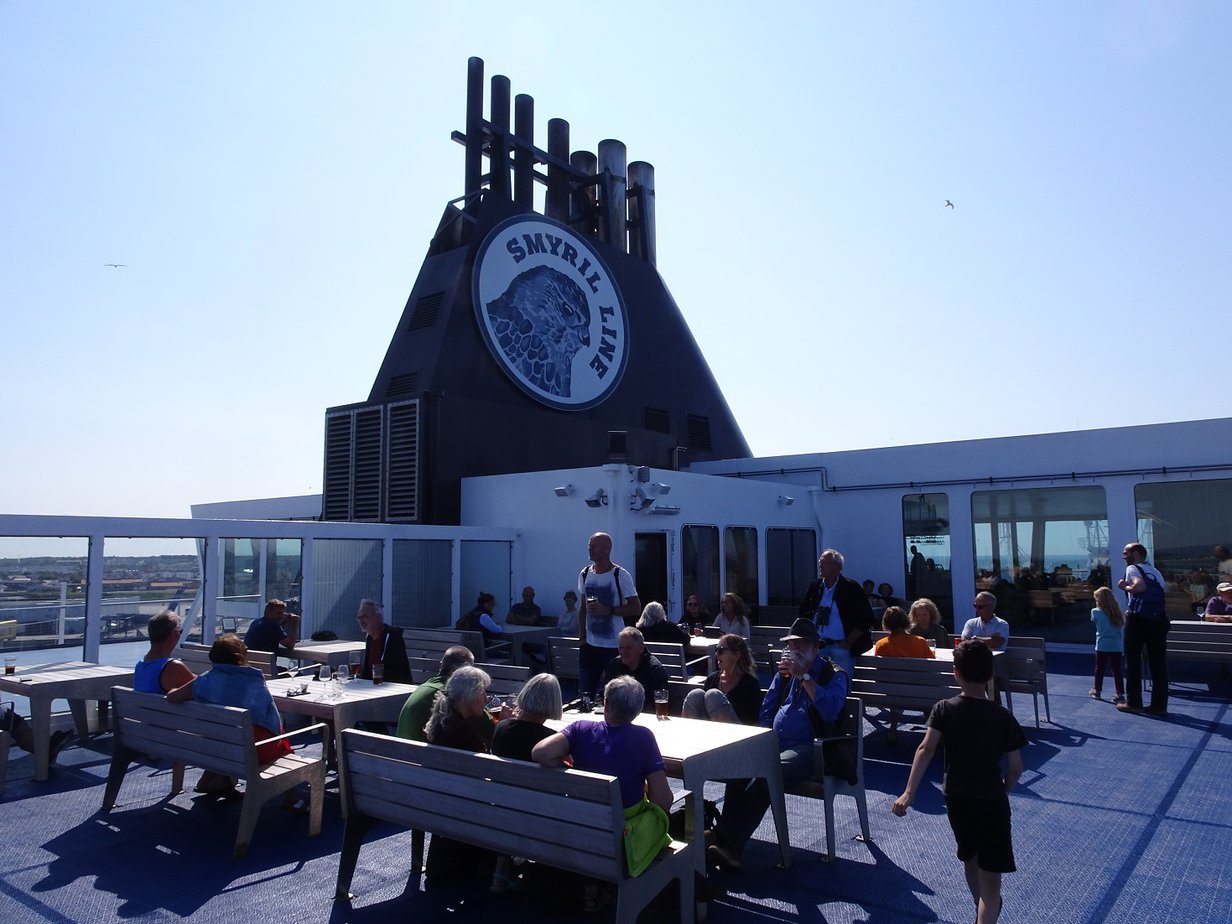 The deck of a boat with people sitting at wooden tables