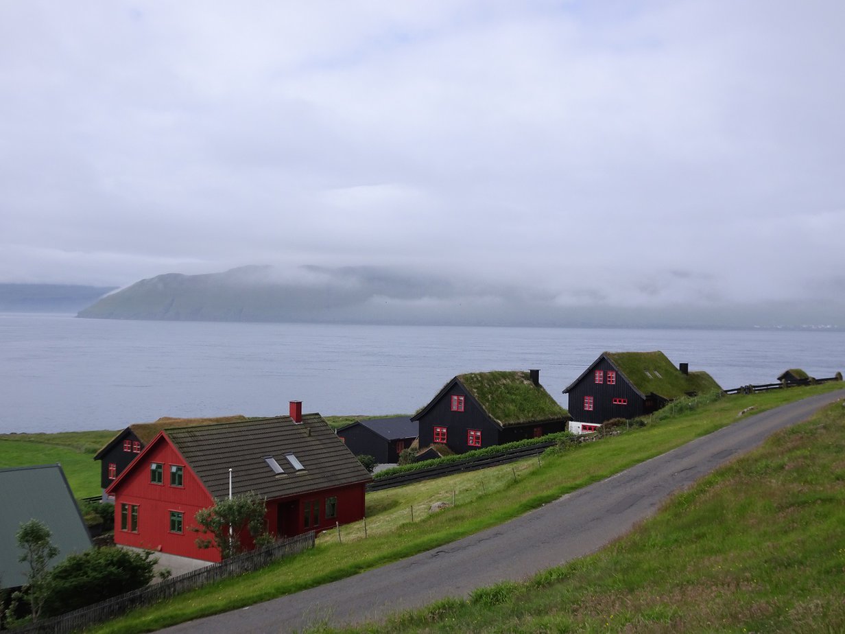 Grass-roofed wooden houses by the Ocean with a road running next to them