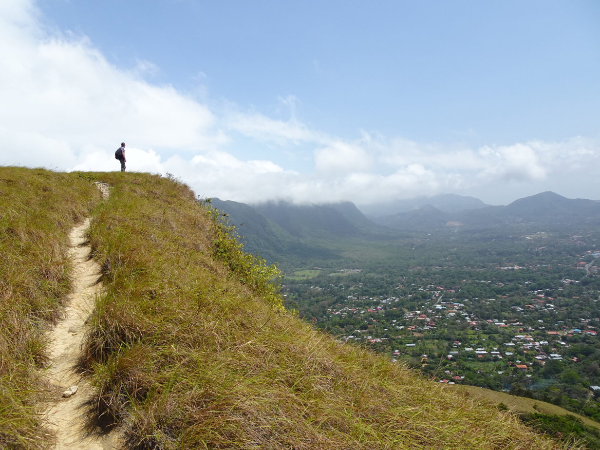 A man standing on a grassy hill high over a valley