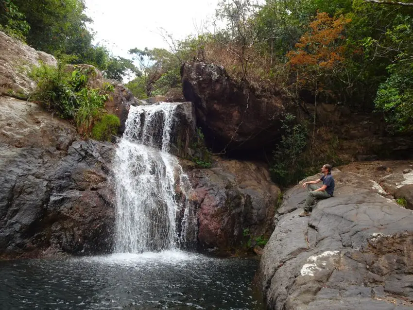 A man sitting on a rock looking at a waterfall