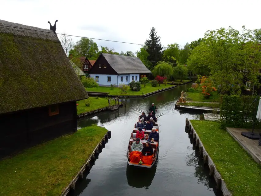 A group of people in a boat on a canal surrounded by small houses and gardens