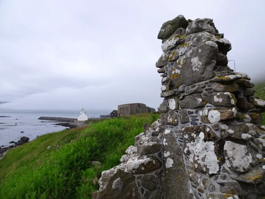 A stone wall by the sea with a whitewashed stone church in the background