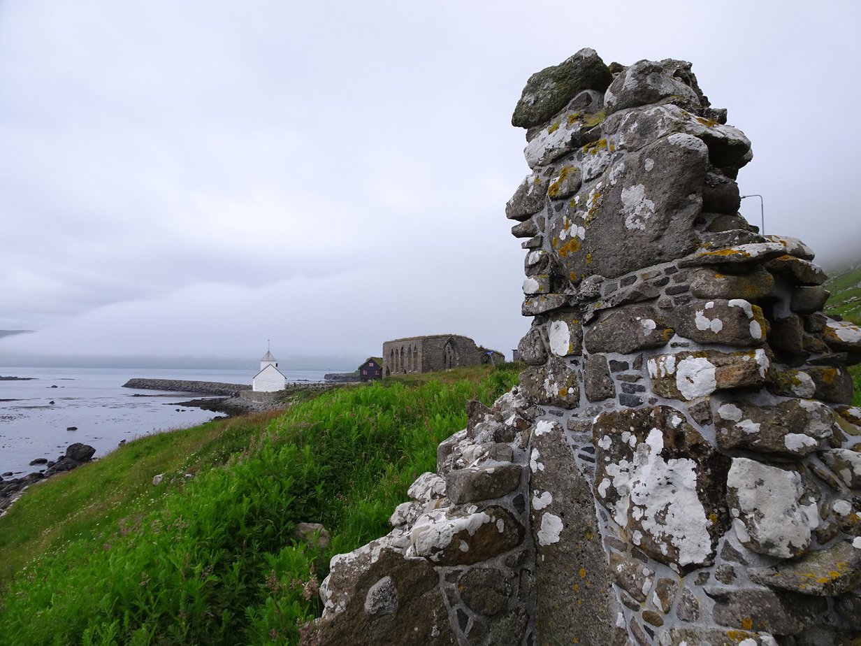 A stone wall by the sea with a whitewashed stone church in the background