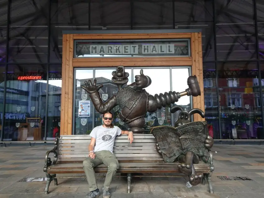 A man sitting on a bench surrounded by statues of Wallace and Gromit