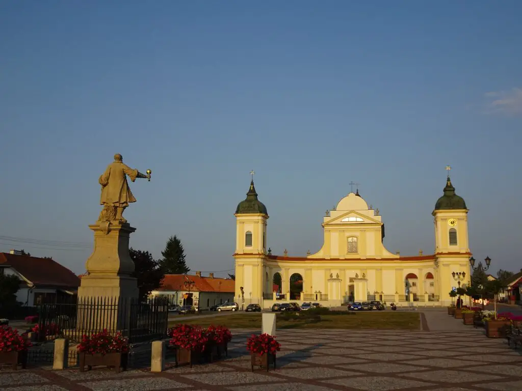 The broad facade of a yellow stone church with a statue in the foreground