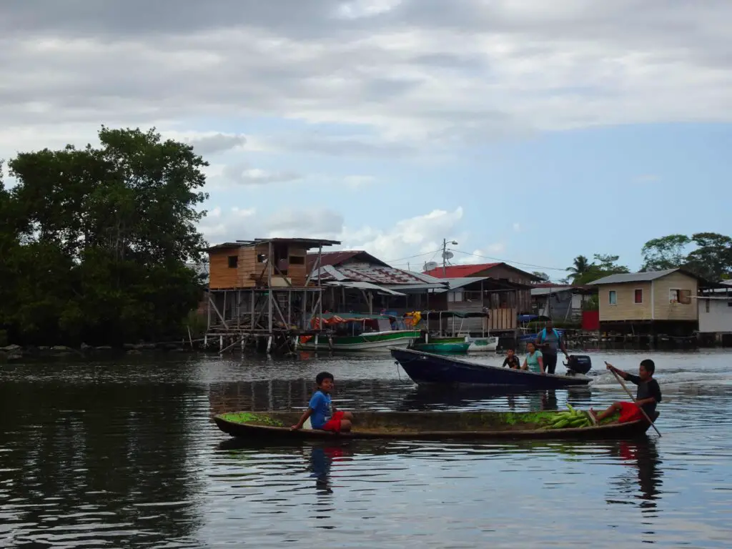 Two children in a wooden boat in front of a stilted wooden house