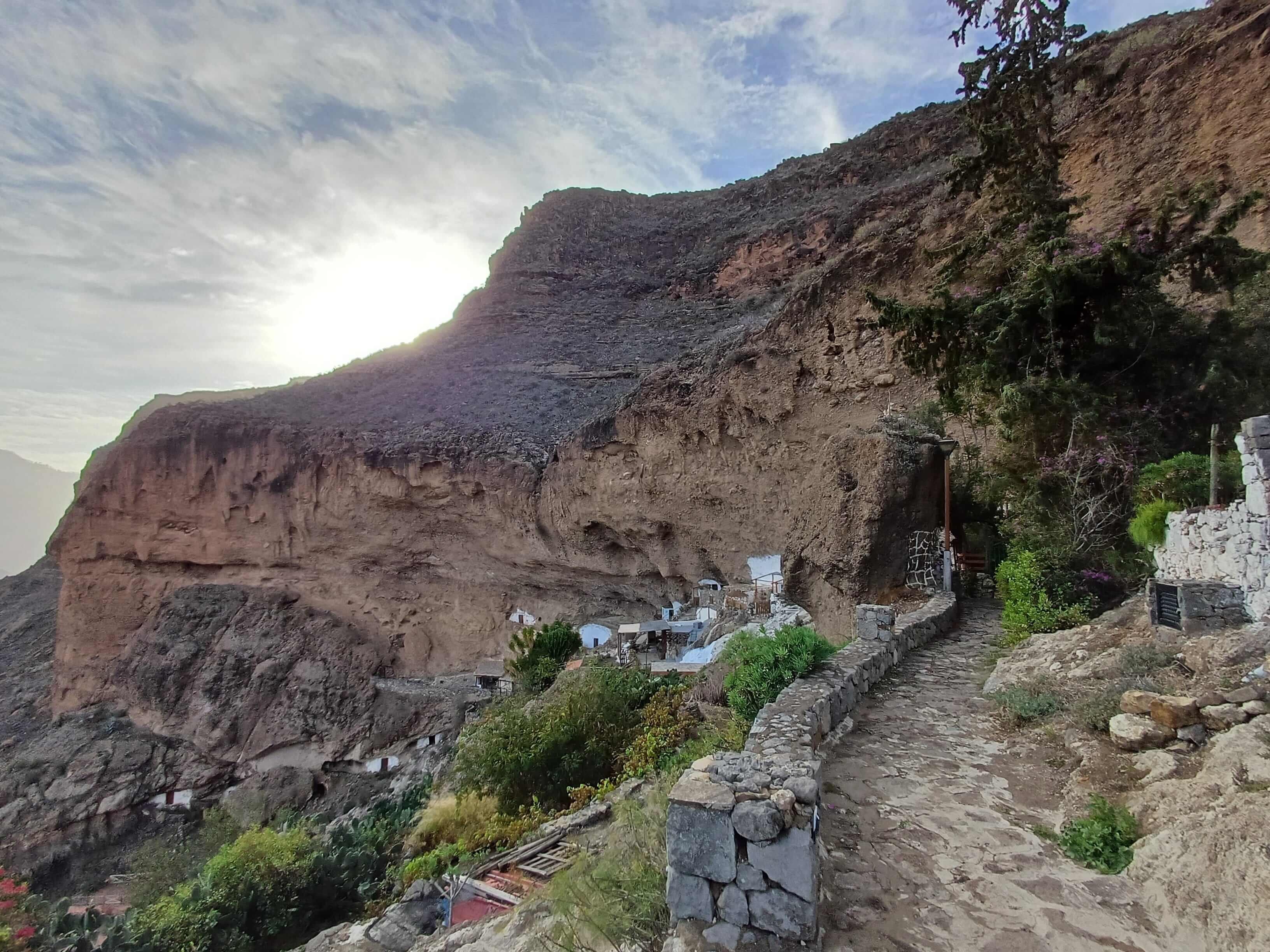 A tall cliff with artifical cave-homes cut in the side of it and a small path leading to the cliff