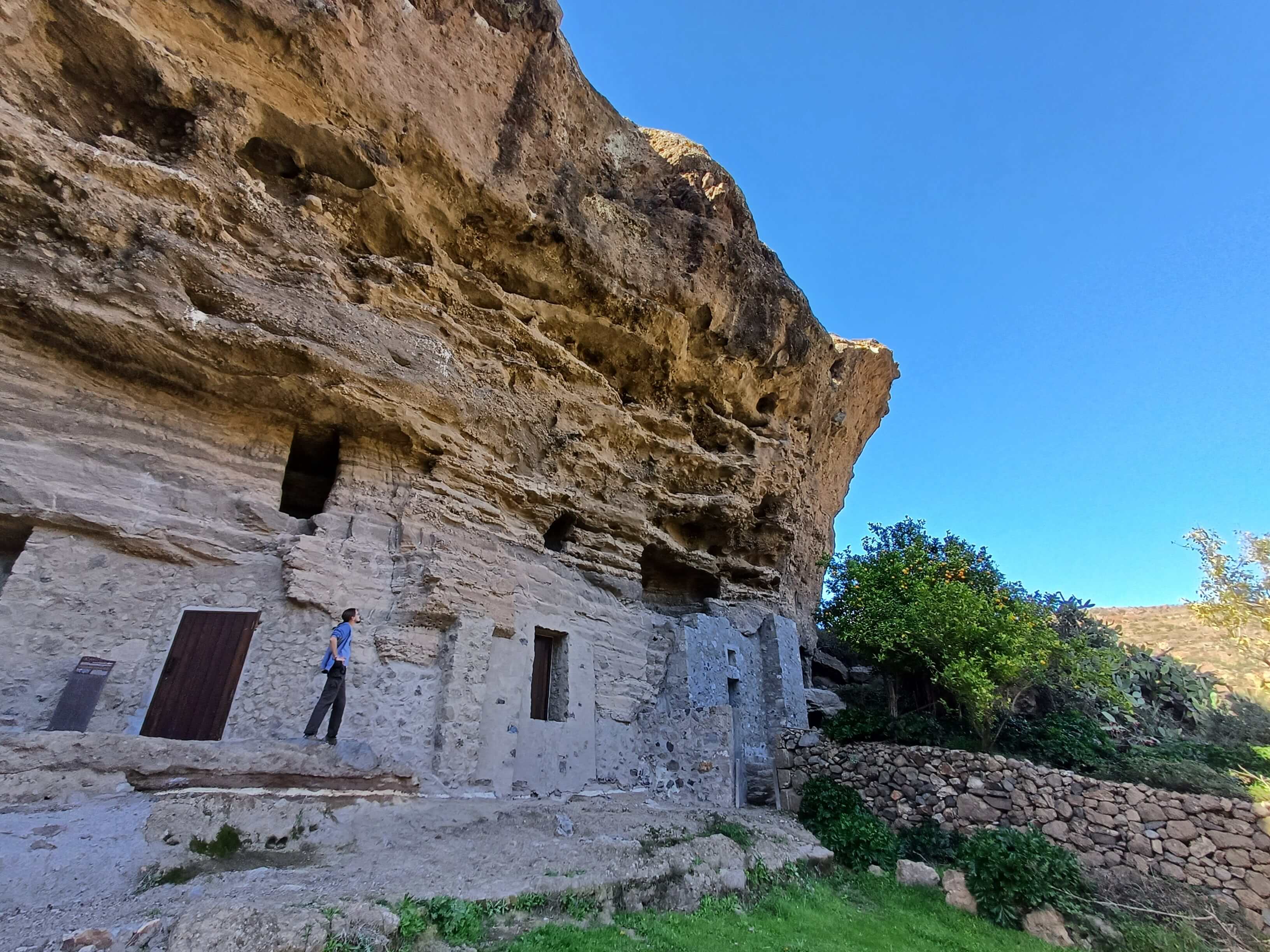 A man standing near a cliff with artificial cave-homes cut in the side of it