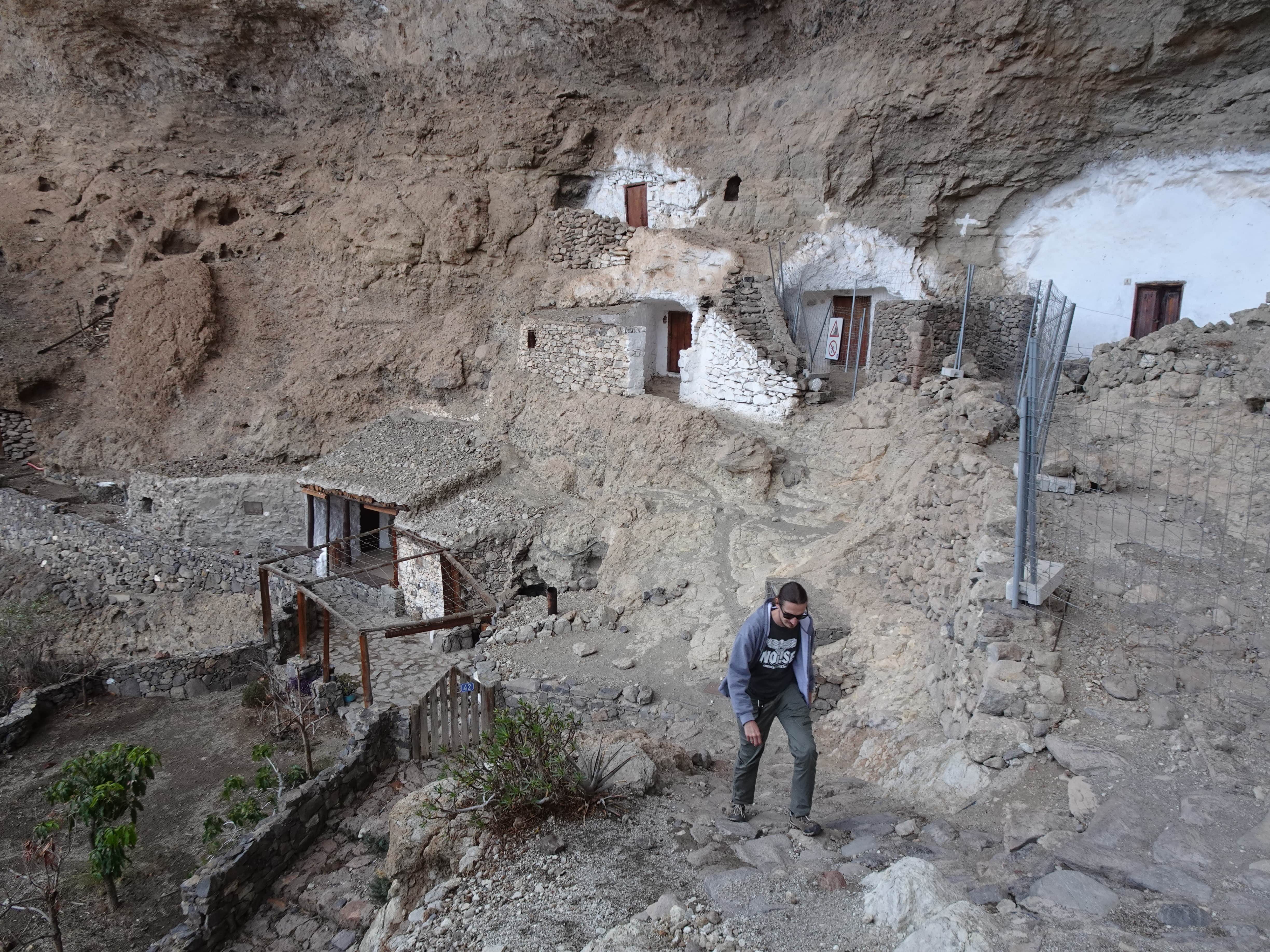 A man walking in front of a cliff with artificial cave-homes cut in the side of it