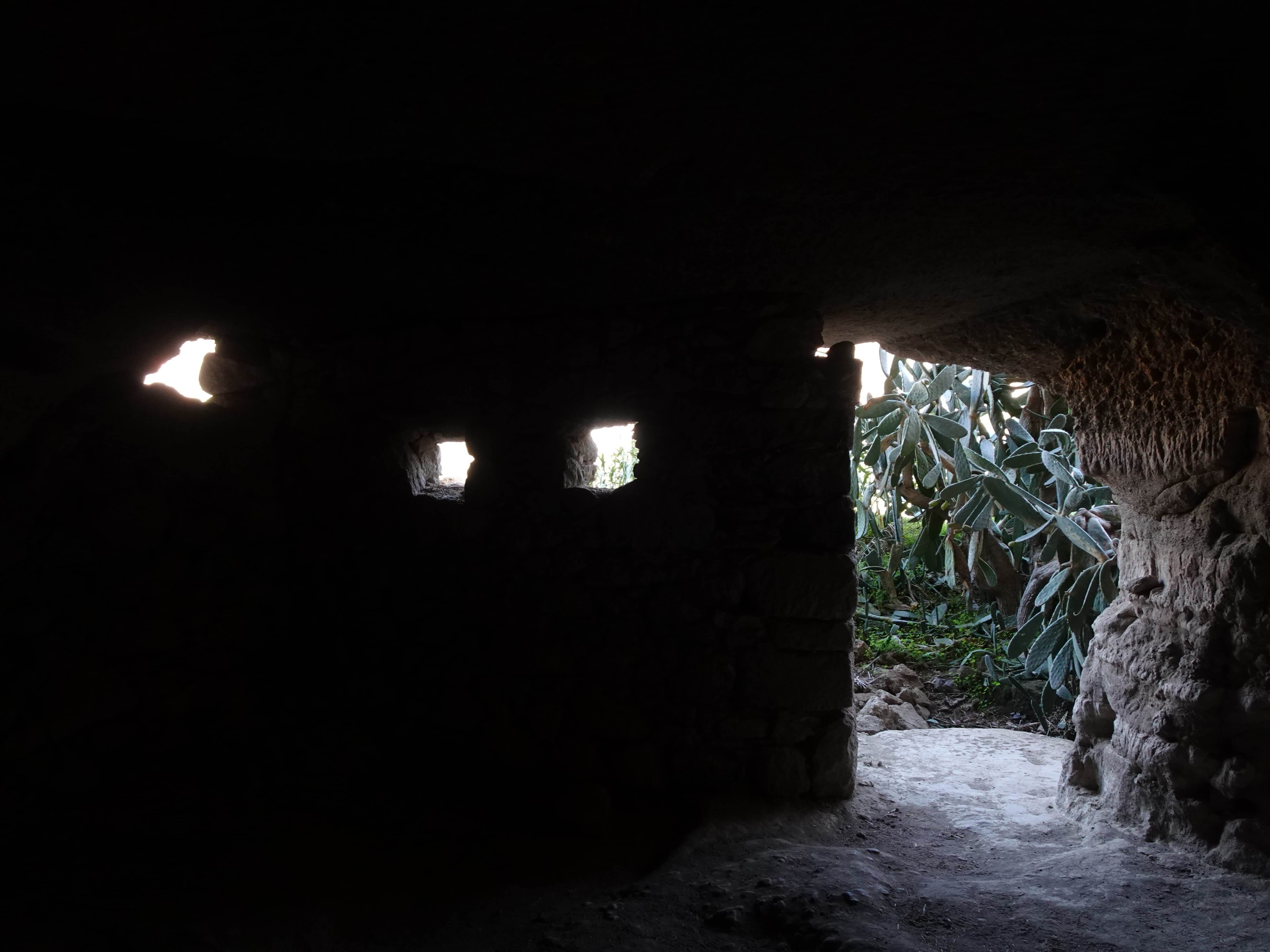 A cave opening and a brick wall with small window openings seen from inside