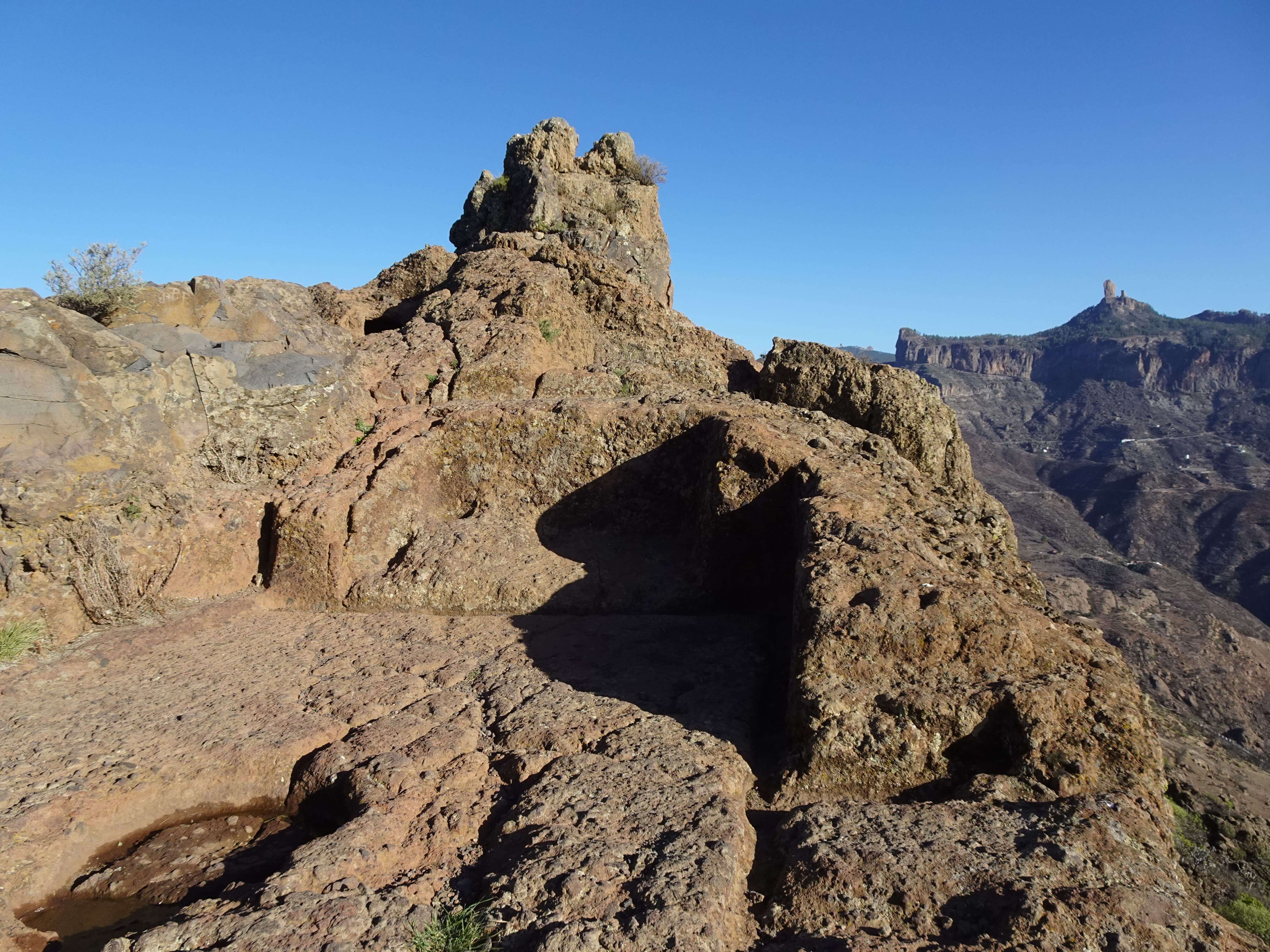 A prehistoric platform cut out of a rock with a rocky outcrop in the background