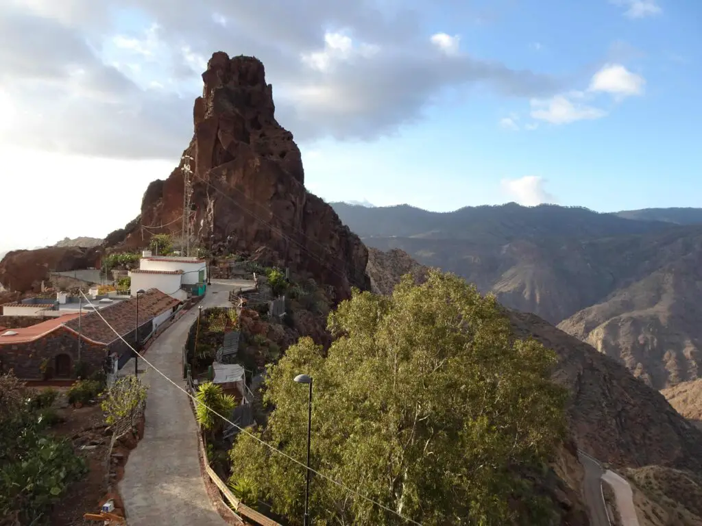 A rock promontory wih small houses at its foot and mountains in the background