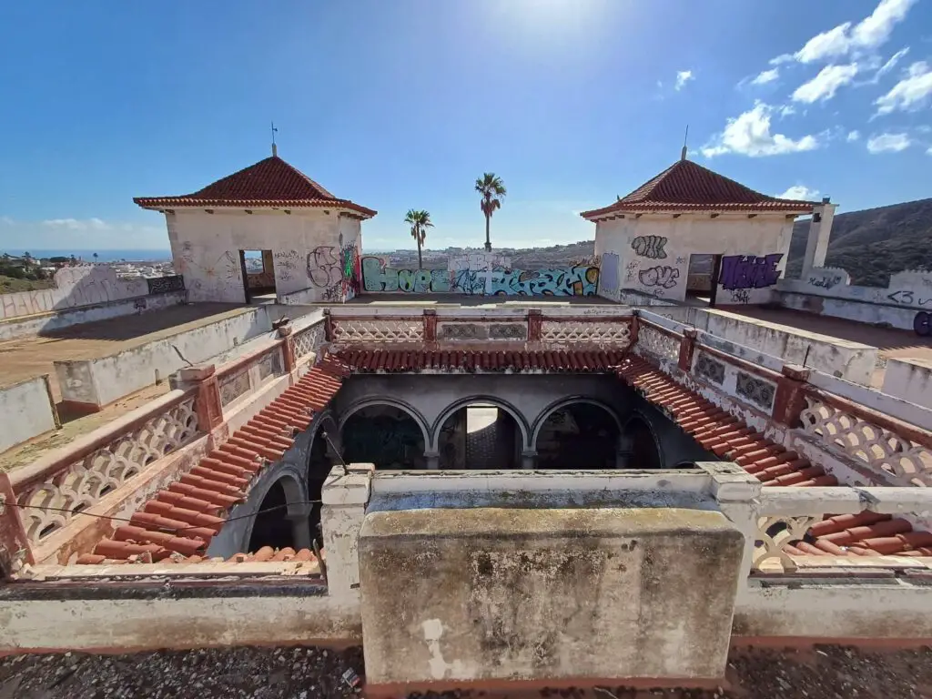 The roof of an abandoned mansion with palm trees in the background