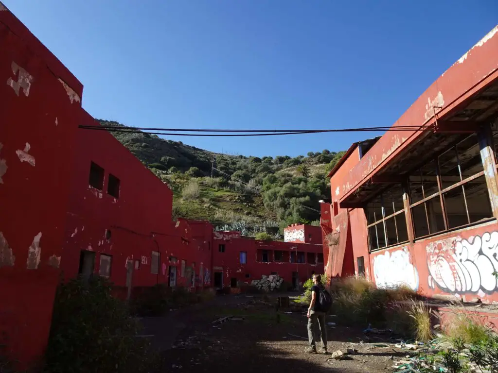 A man standing between two abandoned red-painted buildings