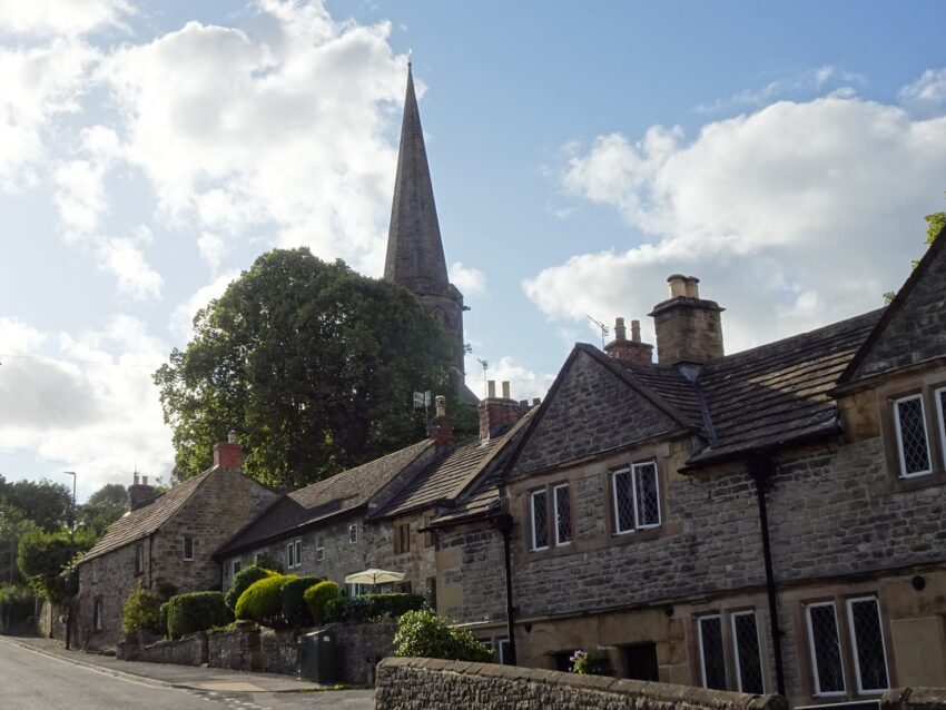Charming historic stone cottages in a picturesque village with a church steeple in the background.