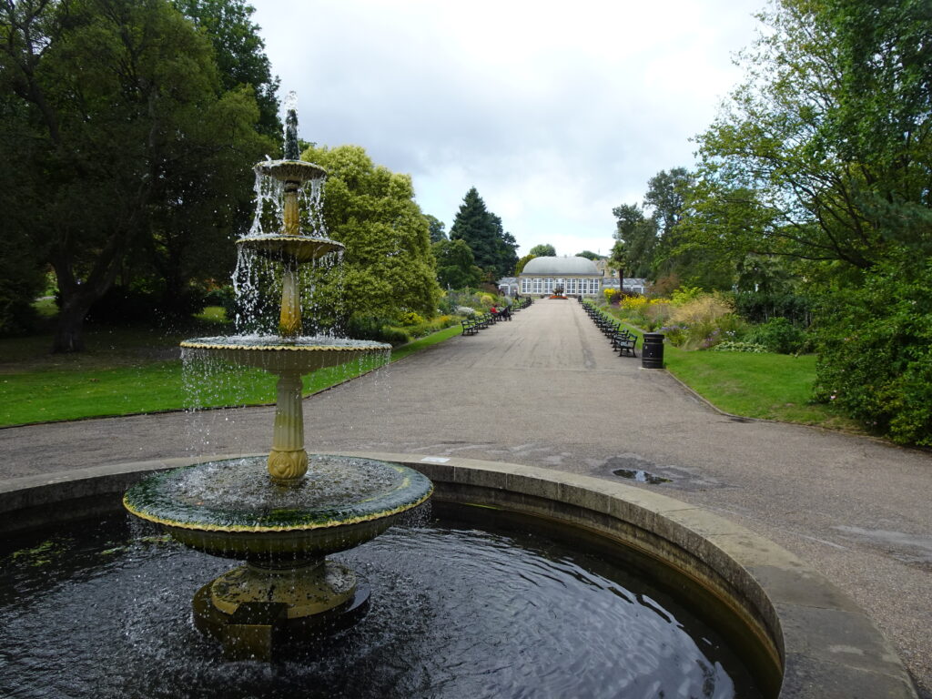 An avenue in a garden with a fountain in the foreground