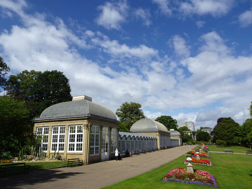 A victorian glasshouse in a garden with blooming flowers growing in front
