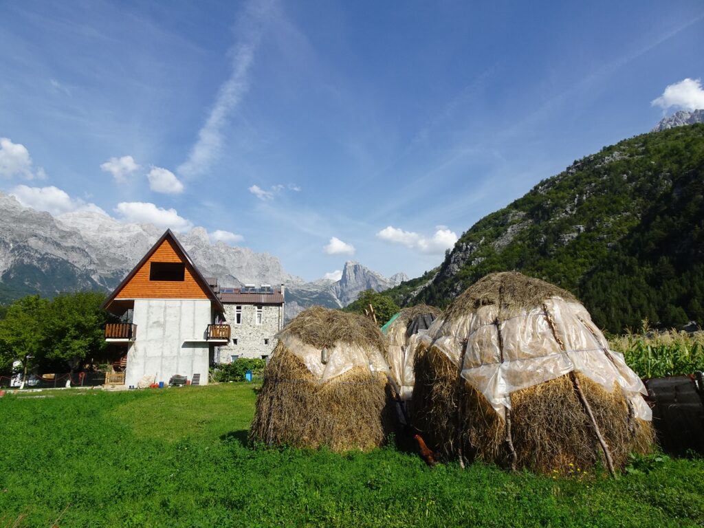 A wooden house in a mountain valley with haybales in the foreground