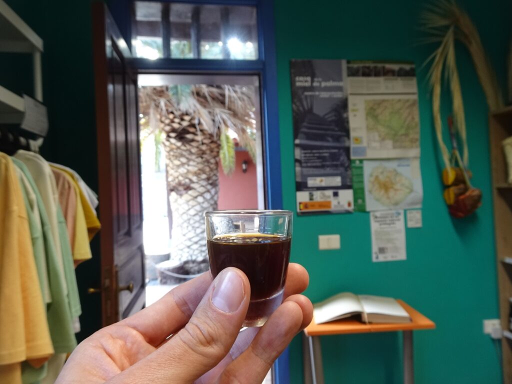 A hand holding a shot glass filled with a dark brown liquid