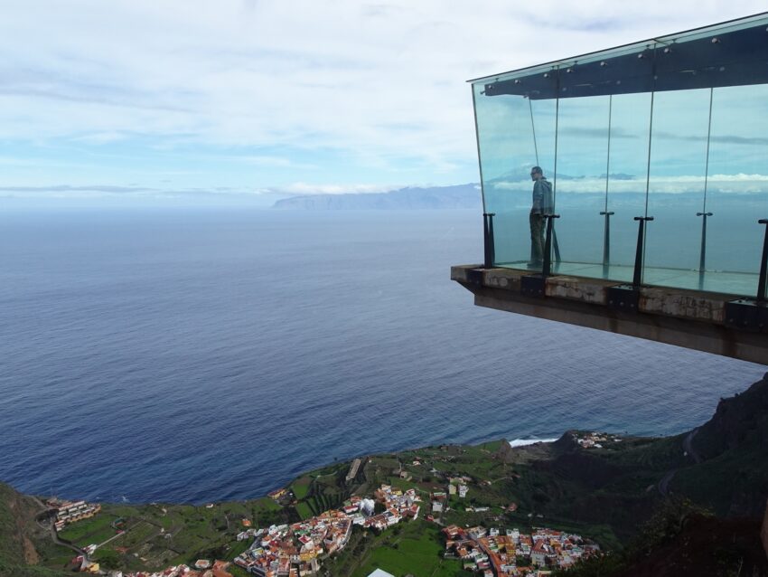 A man standing in an enclosed glass viewpoint jutting out over a cliff