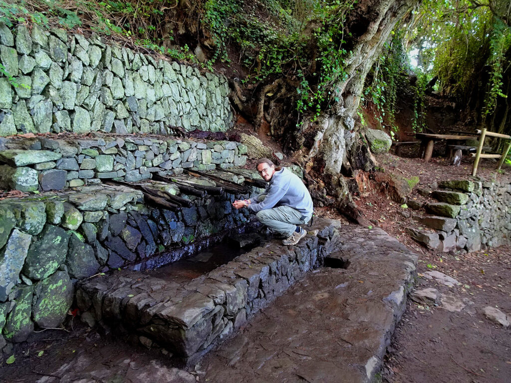 A man crouching at a natural spring, catching water in his hands