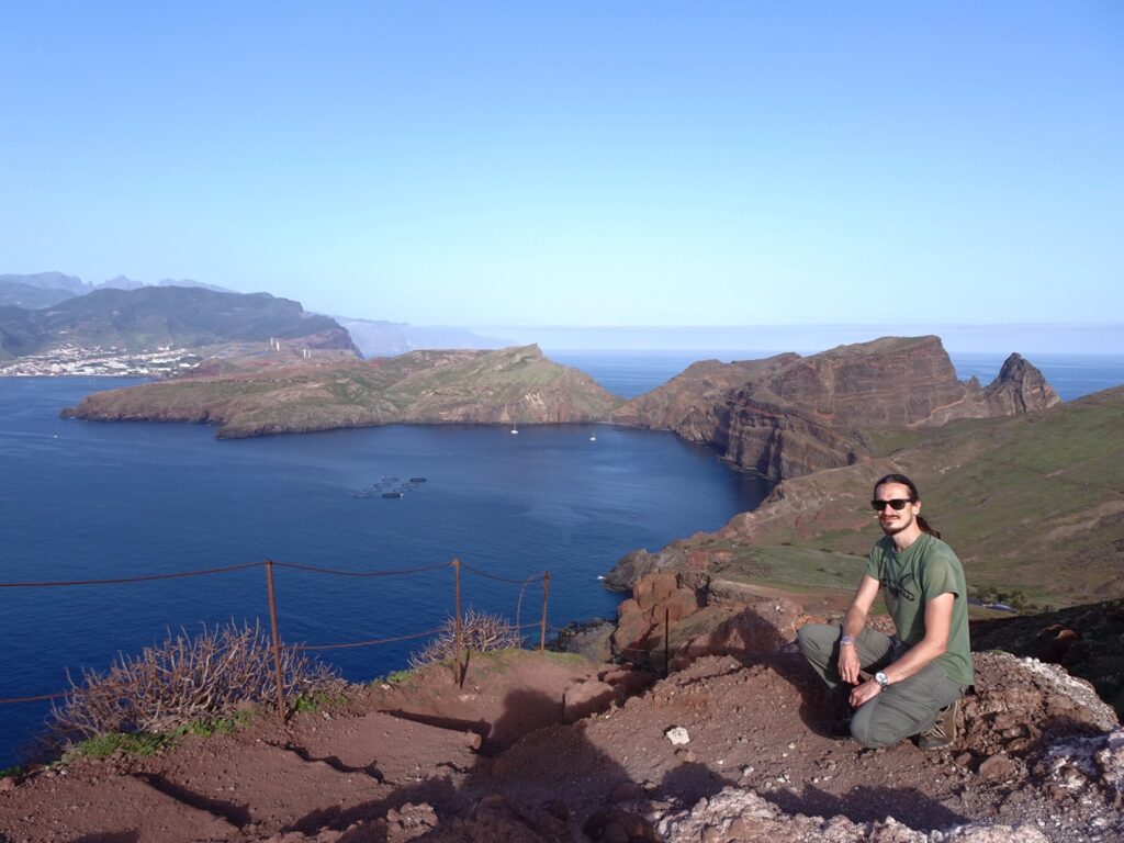 A man sitting in front of long peninsula with sea stacks rising out of the Ocean